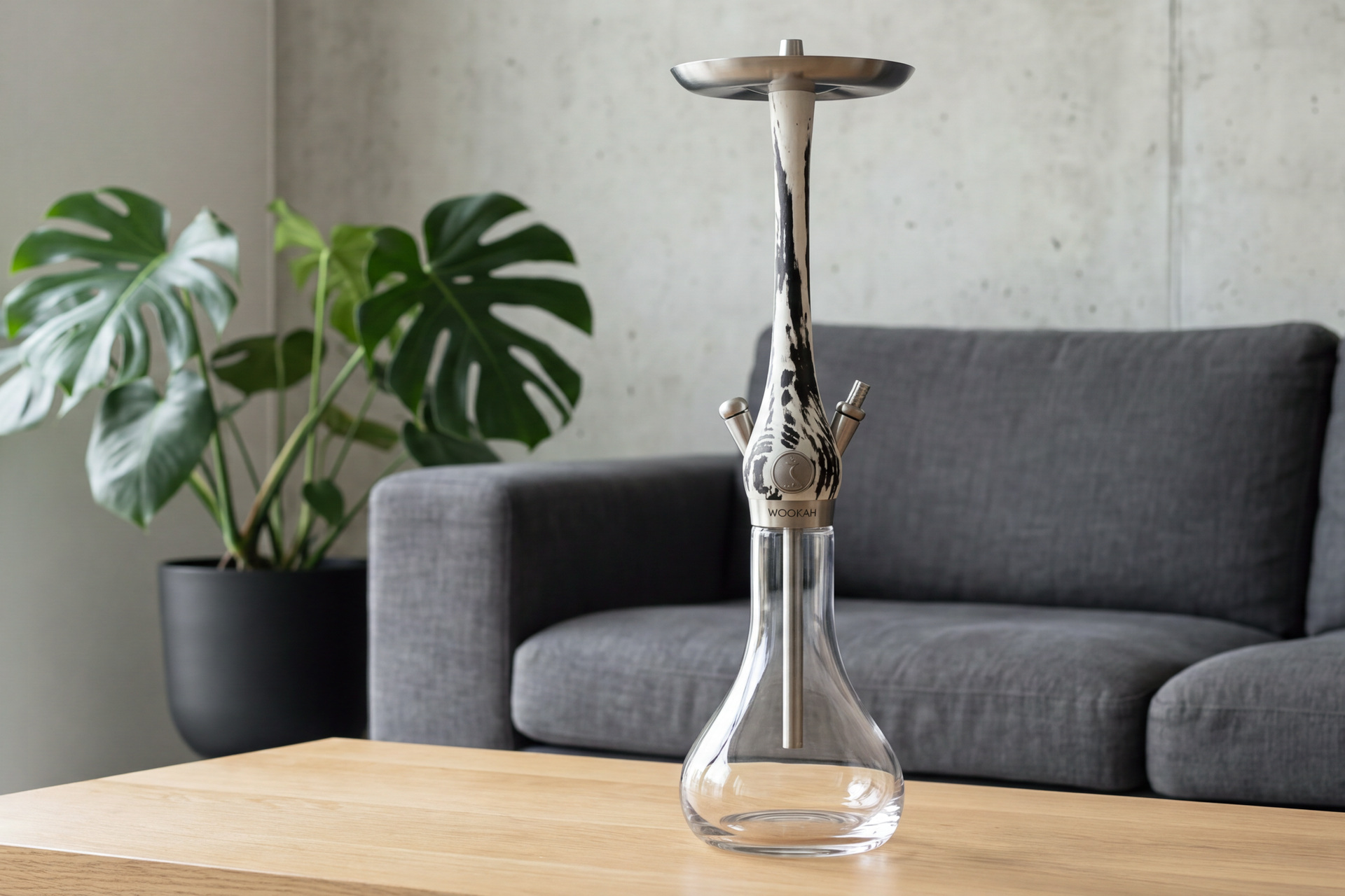 Wei&szlig;-schwarze Rauchs&auml;ule auf klarer Glasvase vor grauem Sofa in einem hellen Loft mit Betonwand
