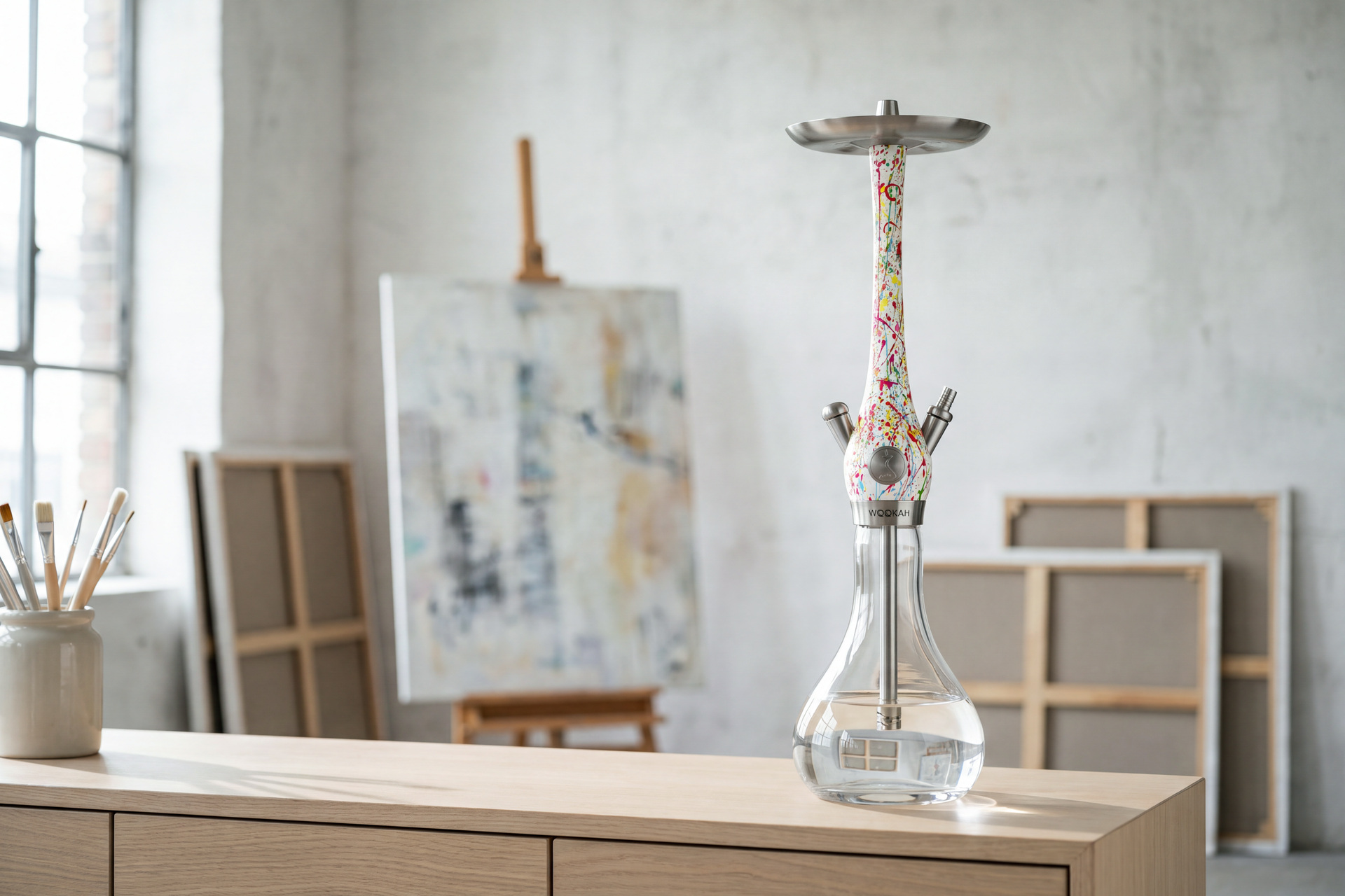 Wookah Body Abstract mit bunt bespritztem wei&szlig;em K&ouml;rper auf klarer Glasvase, auf einem Sideboard im hellen K&uuml;nstleratelier
